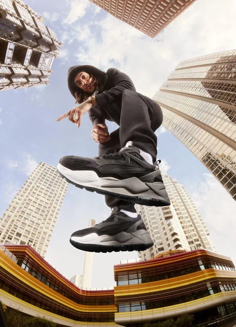 Concept fashion: figura in abiti scuri e sneaker, con architettura urbana